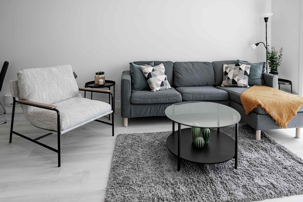A grey couch with a white chair and a glass table in a room.