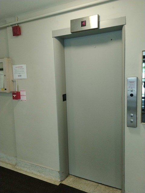 A metal door with a silver handle and a red fire alarm on the wall.