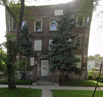 A brick building with a black fence and a tree in front.
