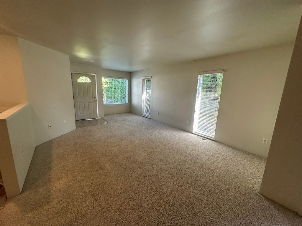 A room with carpeted floor and a door on the left side.