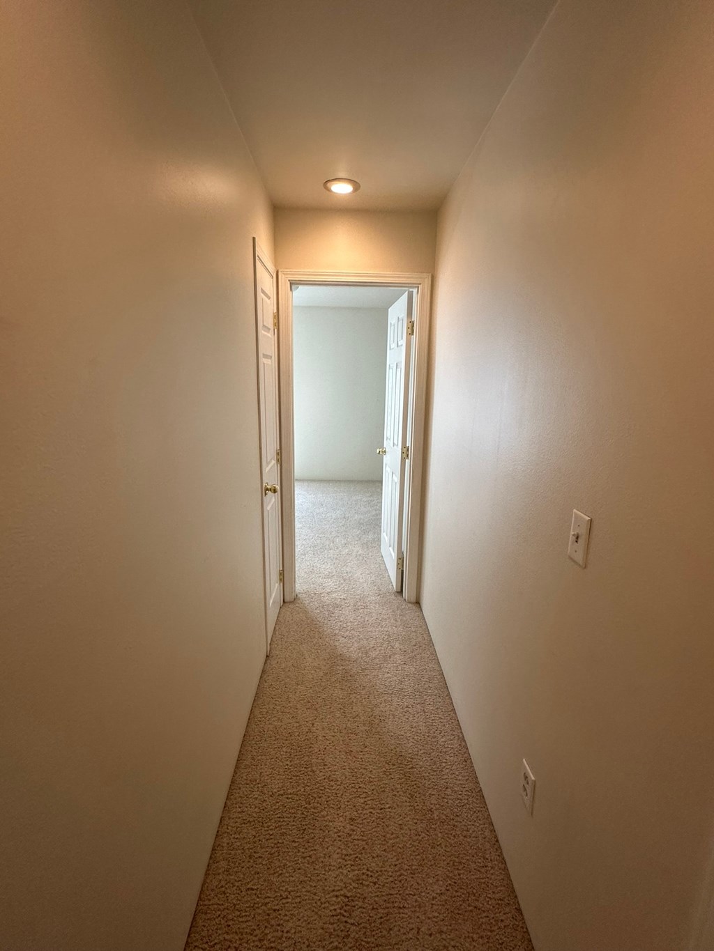 A hallway with a carpeted floor and a light on the ceiling.