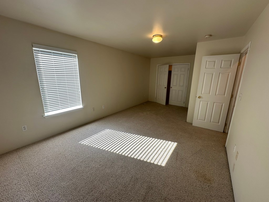 A room with a carpeted floor and a window with blinds.