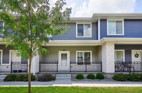A two-story house with a front porch and a tree in front.