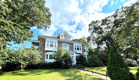 A large white house with a red brick chimney is surrounded by green trees.