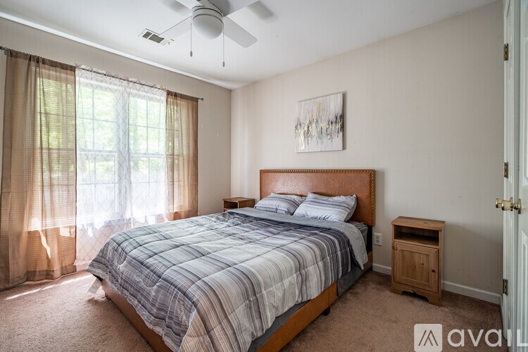 A bedroom with a bed, nightstand, and window with curtains.