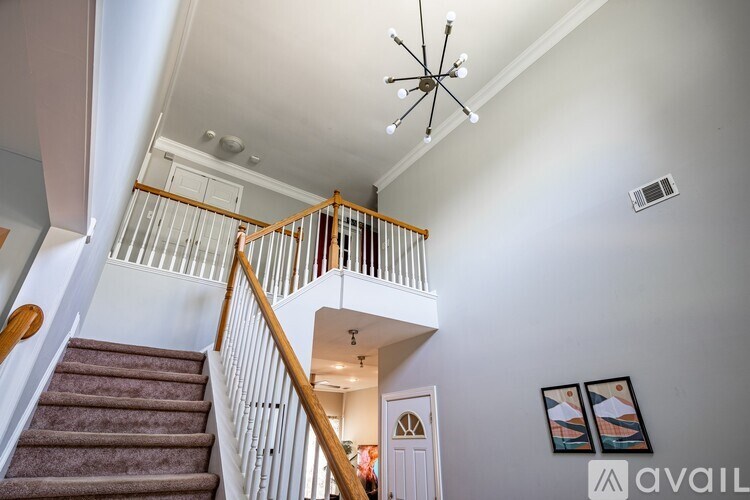 A staircase with a wooden handrail and a carpeted runner leads up to a landing with a chandelier.
