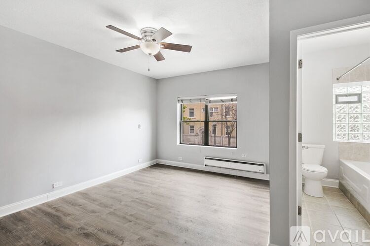 A spacious room with a ceiling fan and a window overlooking a building.