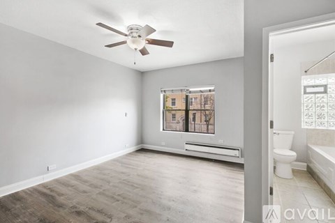 A spacious room with a ceiling fan and a window overlooking a building.
