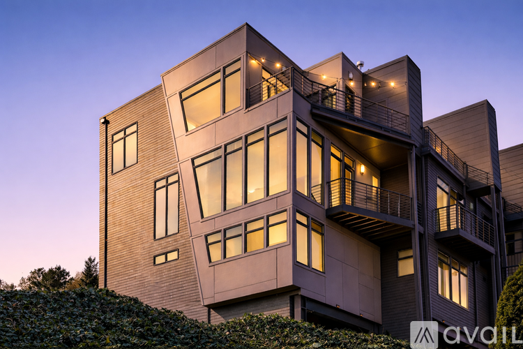 A modern multi-story building with balconies and trees in the foreground.