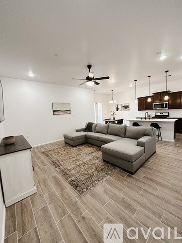 A living room with a grey sofa and a rug in front of a kitchen area.