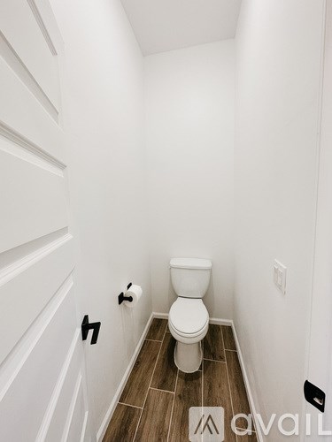 A white toilet in a small bathroom with wood flooring.