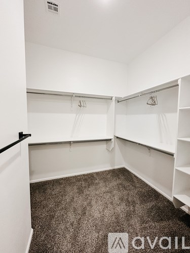 A room with a carpeted floor and white walls, with a row of white shelves and a black door.