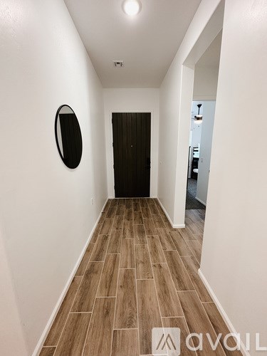 A hallway with wood flooring and a mirror on the wall.