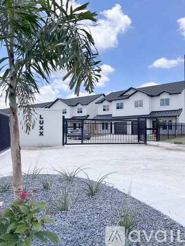 A white house with a black gate and a tree in front.