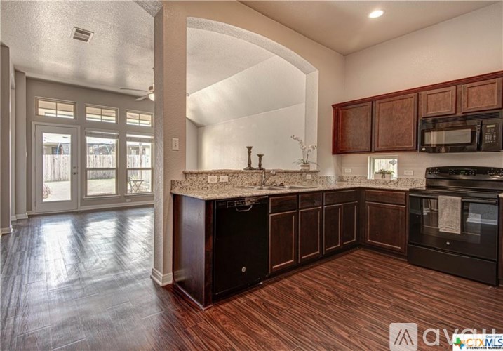 A kitchen with dark wood cabinets and a black dishwasher.