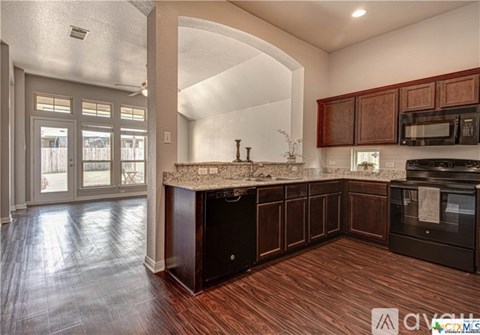 A kitchen with dark wood cabinets and a black dishwasher.