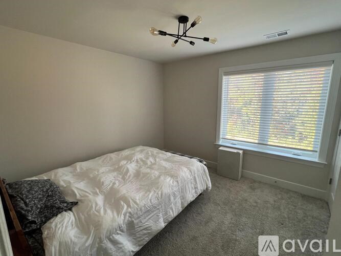 A bedroom with a bed, window, and a chandelier.