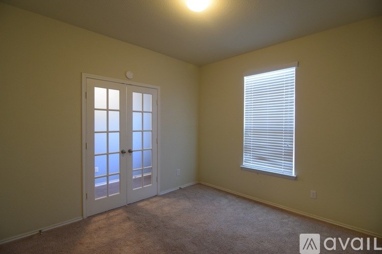A room with a carpeted floor, a window with blinds, and a door leading to a balcony.