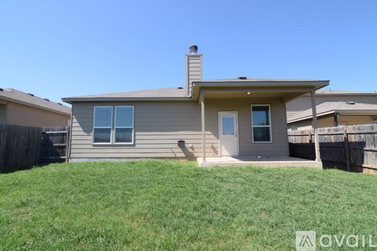 A house with a brown roof and a grey wall is surrounded by a green lawn.