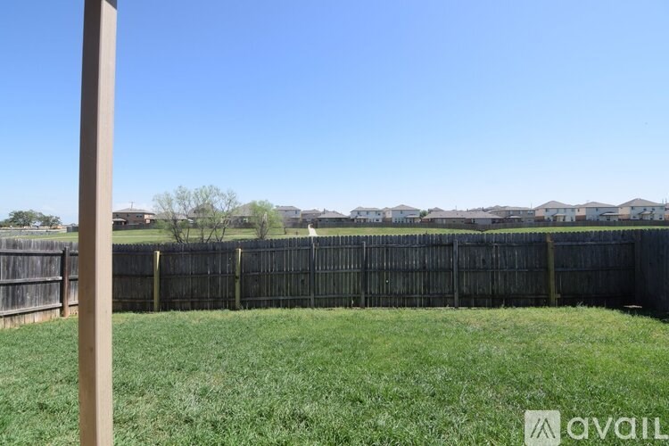 A grassy field with a fence and houses in the distance.