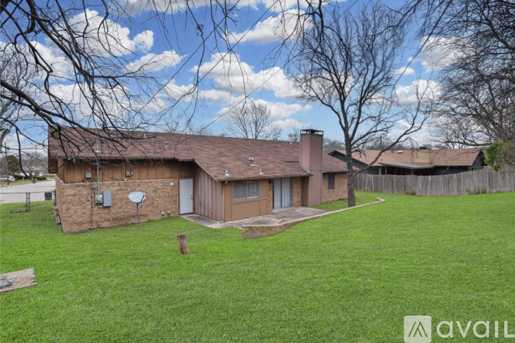 A house with a brown roof and a chimney is surrounded by a fence and trees.