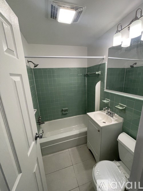 A white toilet is in a bathroom with green tiles.
