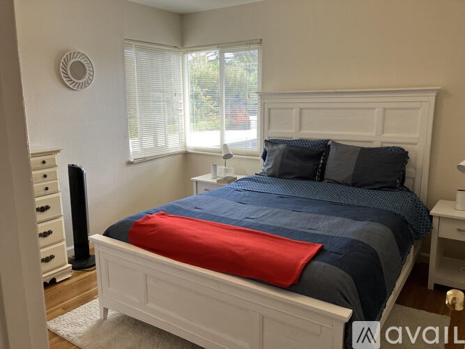 A bed with a blue and red comforter is in a room with a white wall and a window.