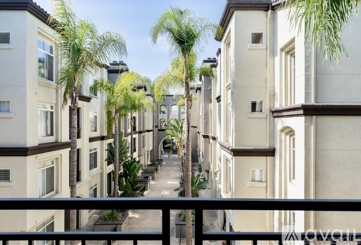 A row of beige buildings with balconies and palm trees in front.