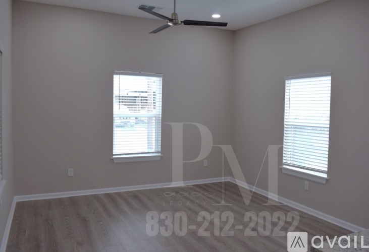 A room with a ceiling fan, two windows with blinds, and a wooden floor.