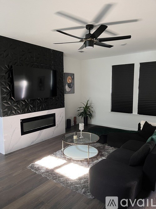 A modern living room with a black couch, a glass coffee table, and a flat-screen TV mounted above a fireplace.