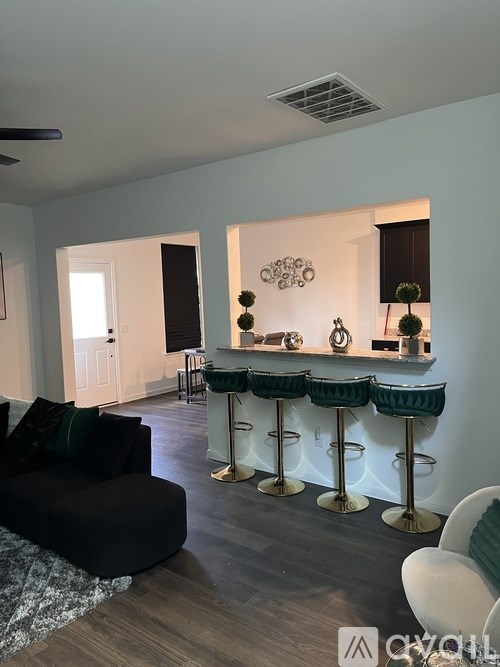 A living room with a black couch and a bar with green stools.