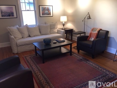 A living room with a white couch, a black chair, and a red rug.