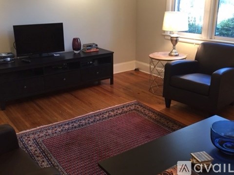 A living room with a black leather chair, a black entertainment center, a red and white rug, and a small white table with a lamp on it.