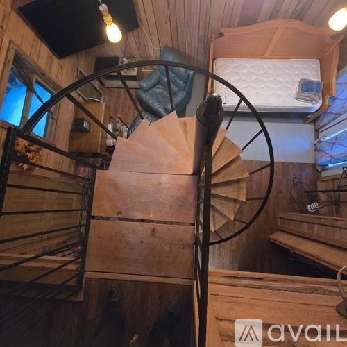 A spiral staircase in a wooden cabin with a bed at the top.
