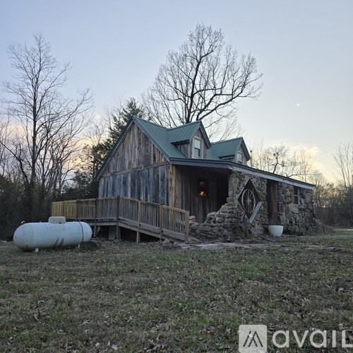 A rustic wooden house with a green roof and a stone chimney is surrounded by bare trees.