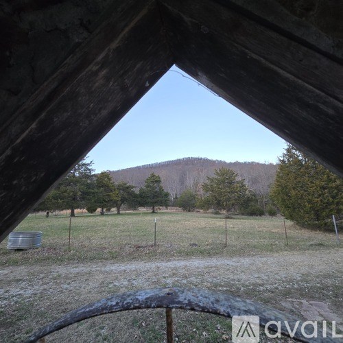 A rustic wooden structure with a view of a field and trees in the distance.