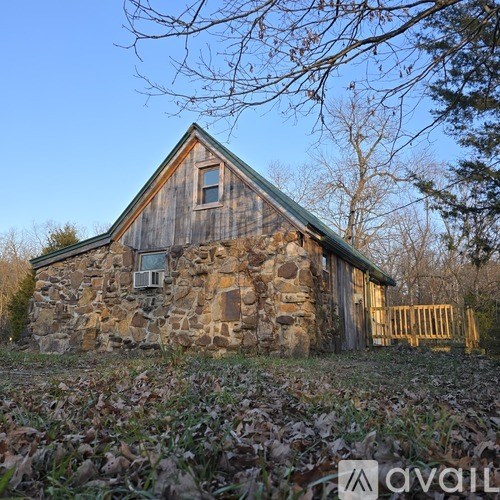 A stone and wood cabin with a green roof and a wooden fence in front.
