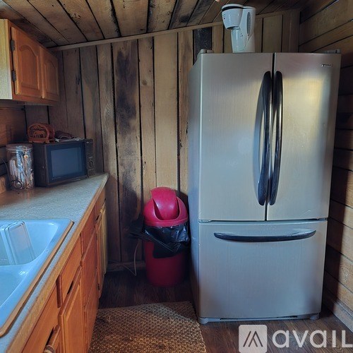 A small kitchen with a white fridge and a red trash can.
