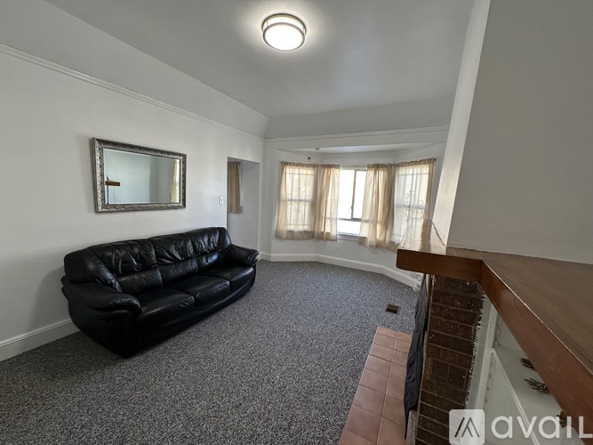 A black leather couch sits in a room with a mirror and a window with curtains.