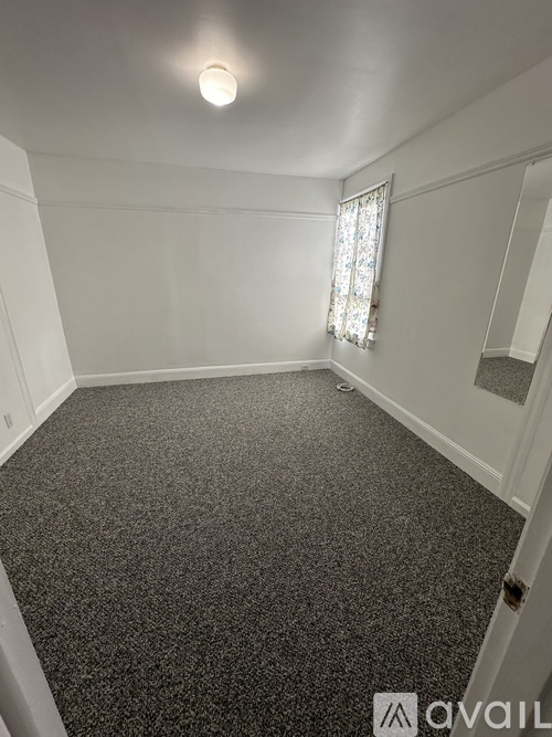 A room with a carpeted floor and a window with curtains.