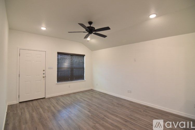 A spacious room with a ceiling fan and a kitchenette in the corner.