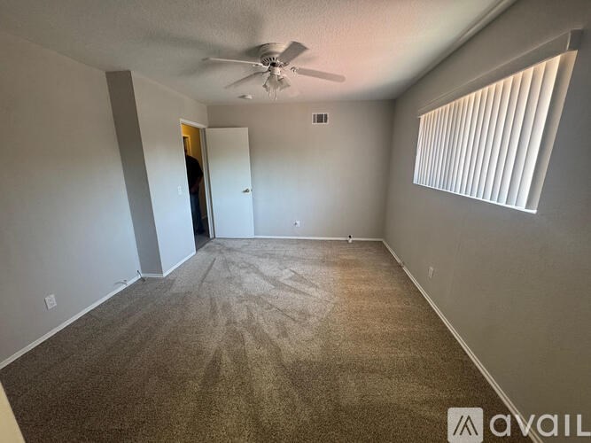 A room with a carpeted floor, a ceiling fan, and a door leading to another room.