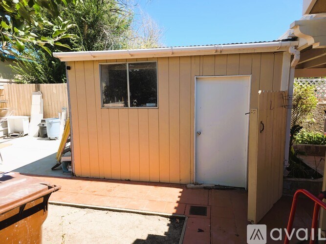 A small wooden shed with a white door and windows is in the foreground with a red handrail to the right.