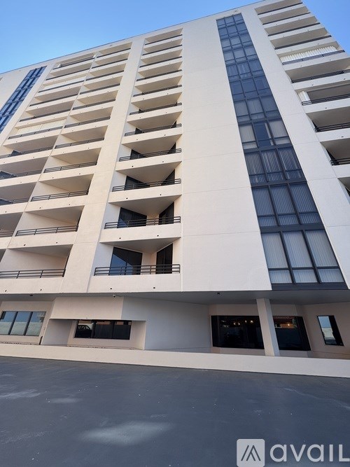 A tall white building with balconies and a blue sky in the background.
