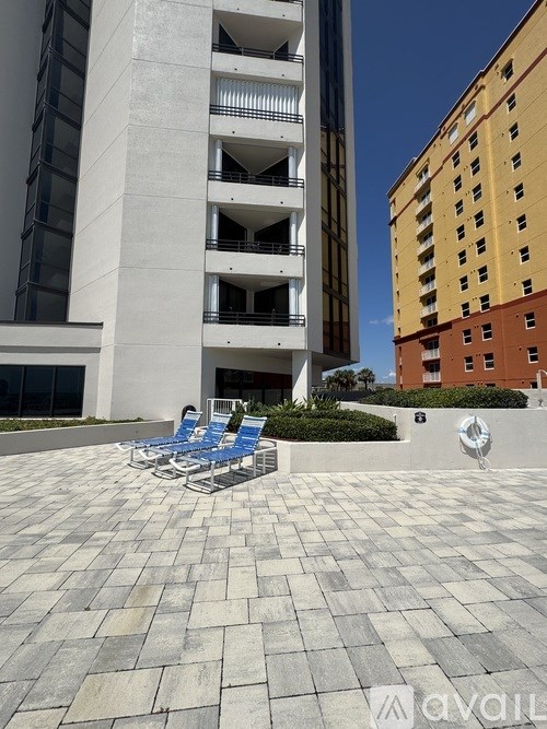 A white building with a balcony and blue chairs in front.