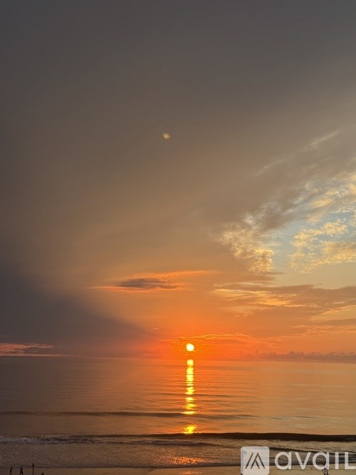 A sunset over the ocean with a few people on the beach.
