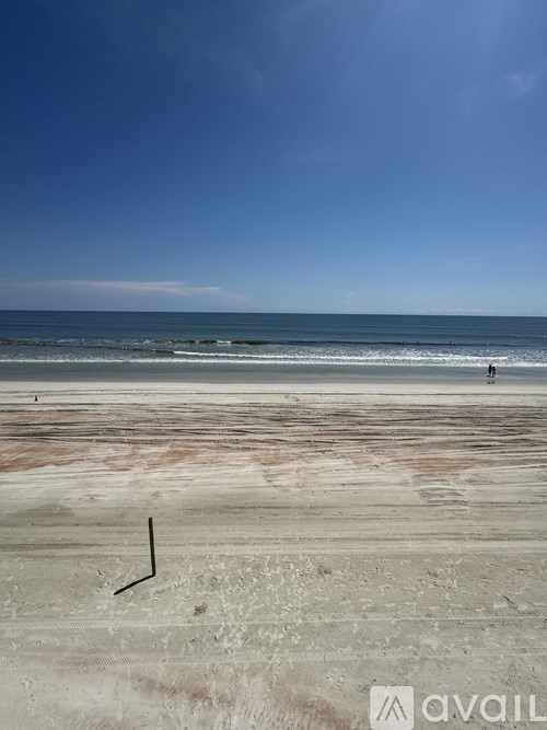 A beach with a person walking in the distance and a stick sticking out of the sand.