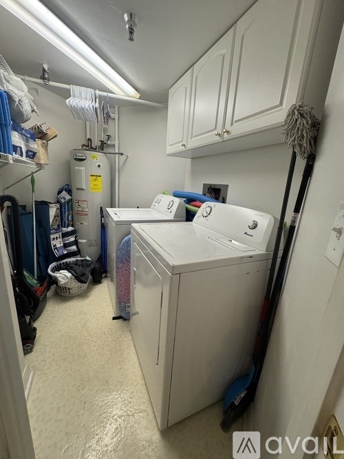 A small, white washing machine is in a cluttered laundry room.