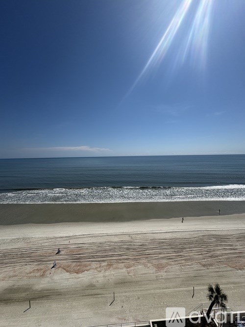 A beach with people walking on the sand and the ocean in the background.