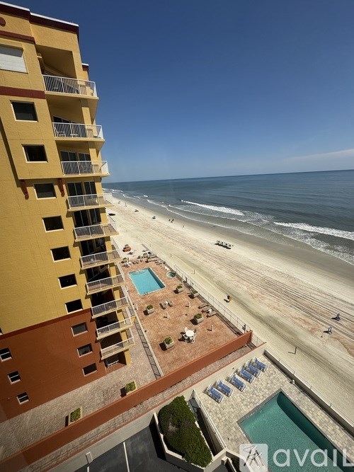 A beachfront apartment complex with a pool and beach in the background.